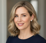 Woman with blonde hair and blue eyes wearing a dark top against a neutral background